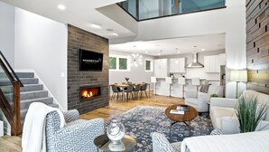 A modern living room with a fireplace, a dining area, and a kitchen. - Lakefront Luxury (Mound)