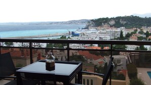 A balcony with a table and chairs, overlooking a coastal cityscape with buildings and a beach. - ONE OF THE MOST BEAUTIFUL VIEWS OF NICE / MONT BORON / BASSE CORNICHE -  (Nice)
