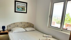 Un lit bien fait, avec du linge de lit et des serviettes blanches, une tête de lit à motifs, une table de chevet avec une lampe et un tableau encadré au mur.