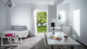 Een moderne, minimalistische woonkamer met een bank, een eettafel gedekt met eten en drinken, en uitzicht op een weelderige tuin door een groot raam.