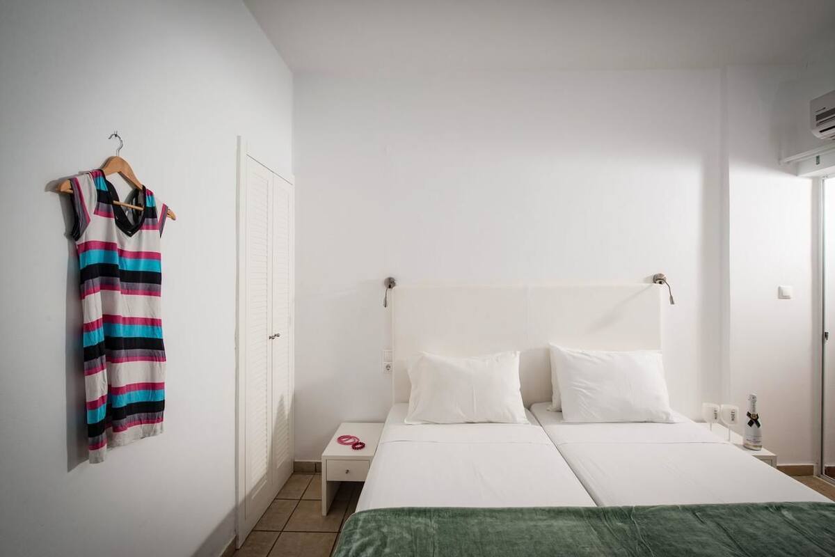 Een hotelkamer met een bed, nachtkastje, kledinghanger en een deur.