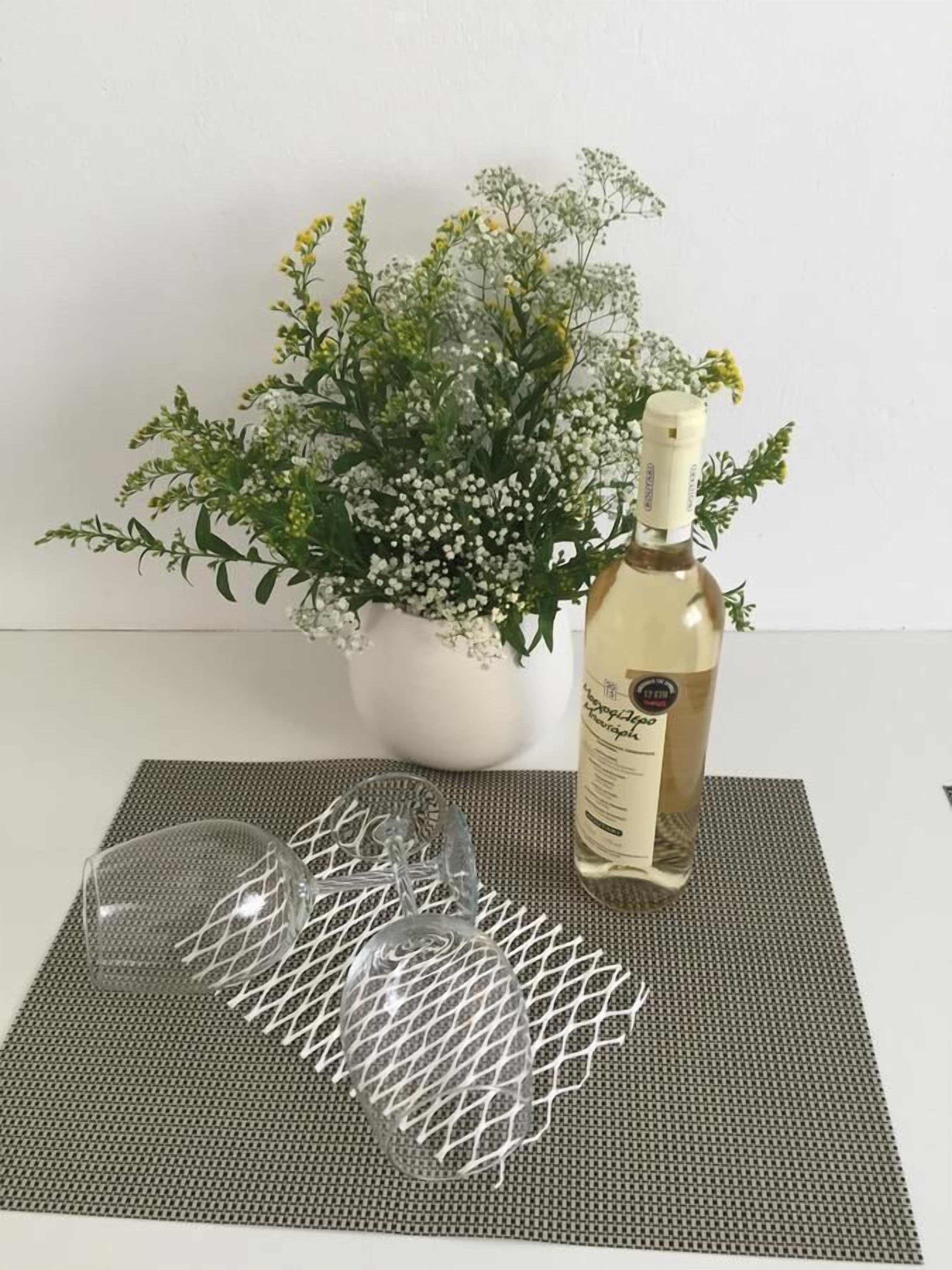 Eine Weinflasche, zwei Weingläser und ein Blumentopf auf einer gemusterten Matte.