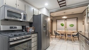 Une cuisine moderne équipée d’appareils électroménagers en acier inoxydable, un coin repas avec une table et des chaises, et une fenêtre avec des stores.