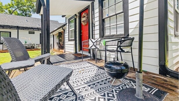 Une terrasse couverte avec des meubles d’extérieur, une porte rouge et un tapis à motifs.