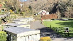 Ein Campingplatz mit Wohnwagen, einer Rasenfläche und einer Hügelkulisse im Hintergrund.