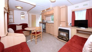 Ein kompaktes Wohnmobil-Interieur mit Küchenzeile, Essbereich, Sitzgelegenheit und Fernseher.