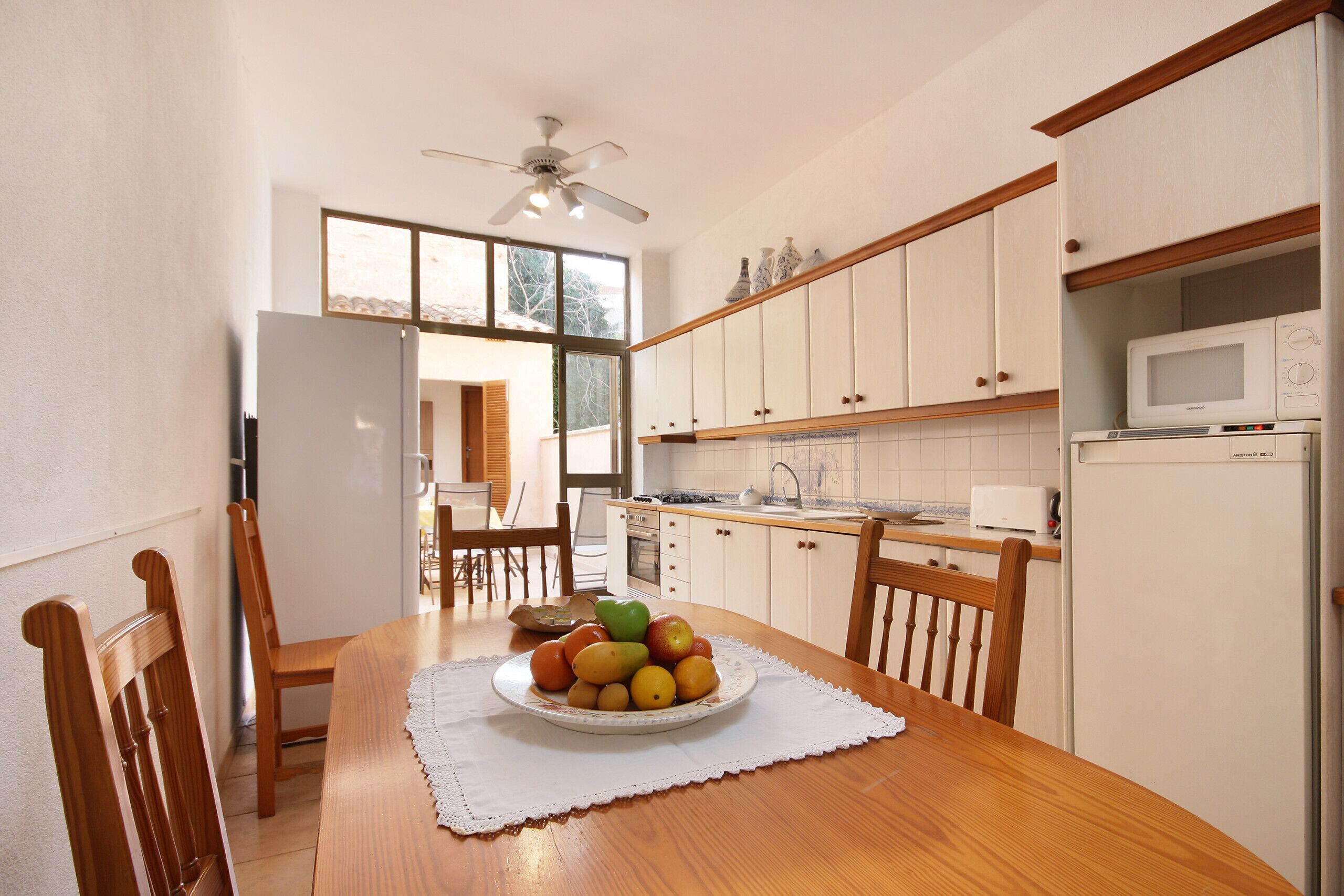 A kitchen with white cabinets, a microwave, and a dining table with a fruit bowl.