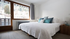 Une chambre avec un grand lit, une fenêtre avec des rideaux, un radiateur et une table de chevet avec une lampe.