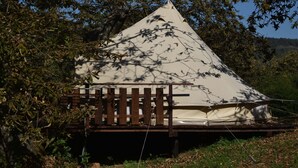 Een tent met een houten bank ervoor, omgeven door bomen.