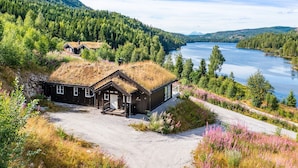 A cabin with a grass roof, surrounded by a forest and a lake.