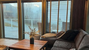 A cozy living room with a large sectional sofa, a wooden coffee table, and a view of a snowy landscape through large windows.