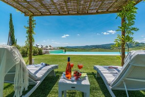 Un espacio al aire libre cubierto con dos sillones, una mesa con una botella y vasos, y vistas a una piscina y paisaje.