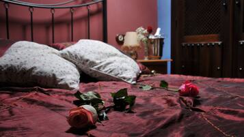 Una cama con una colcha roja, dos almohadas y un florero con flores sobre una mesita de noche.