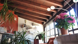 A room with wooden beams on the ceiling, a bookshelf with books, a potted plant, and a window with natural light. - La Casa del Canónigo - Adults Only (Huete)