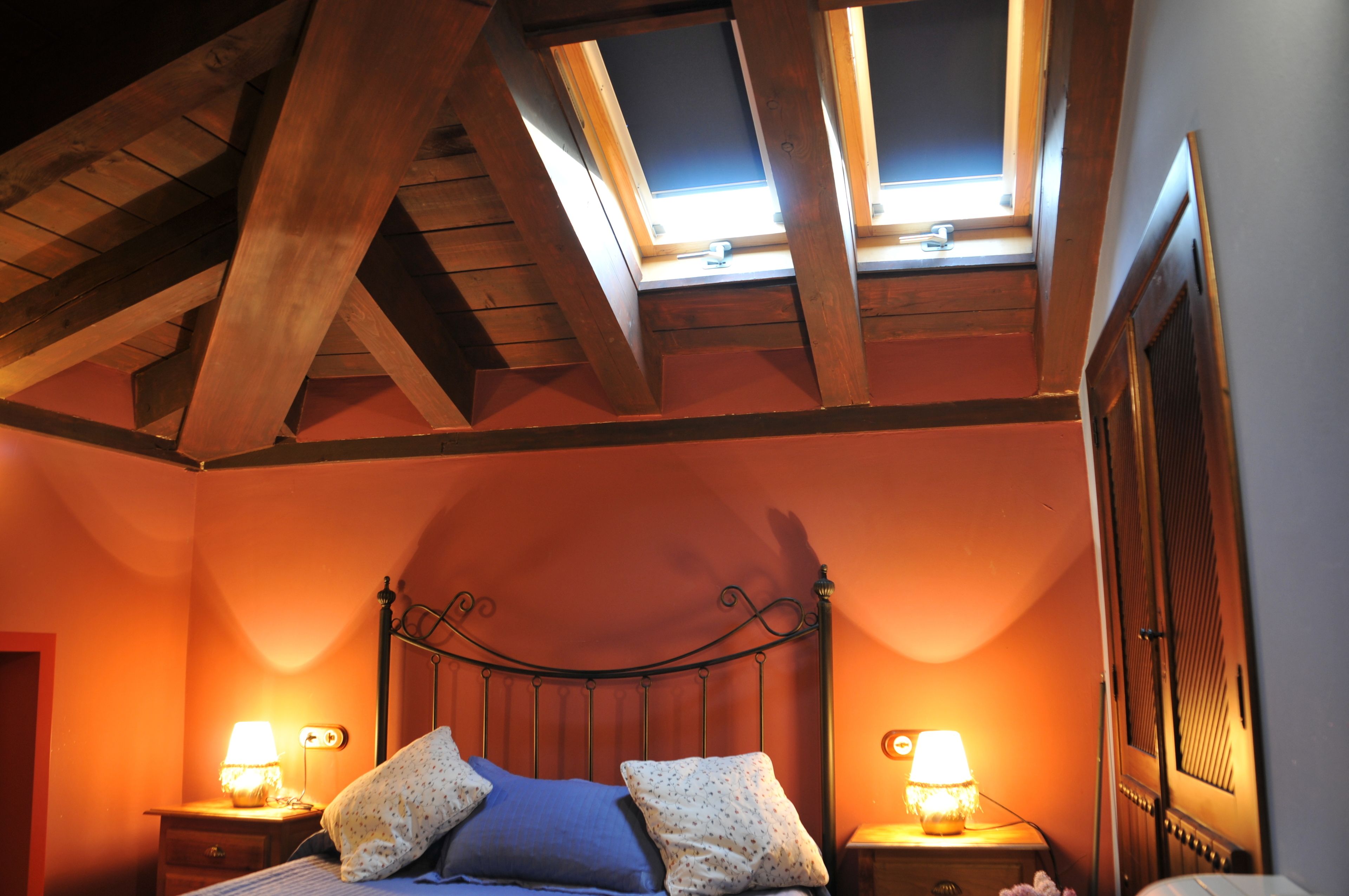 A bedroom with a sloped ceiling, a bed with two pillows, two bedside lamps, and a window with a view of the sky.