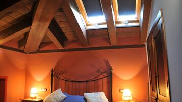 A bedroom with a sloped ceiling, a bed with two pillows, two bedside lamps, and a window with a view of the sky.