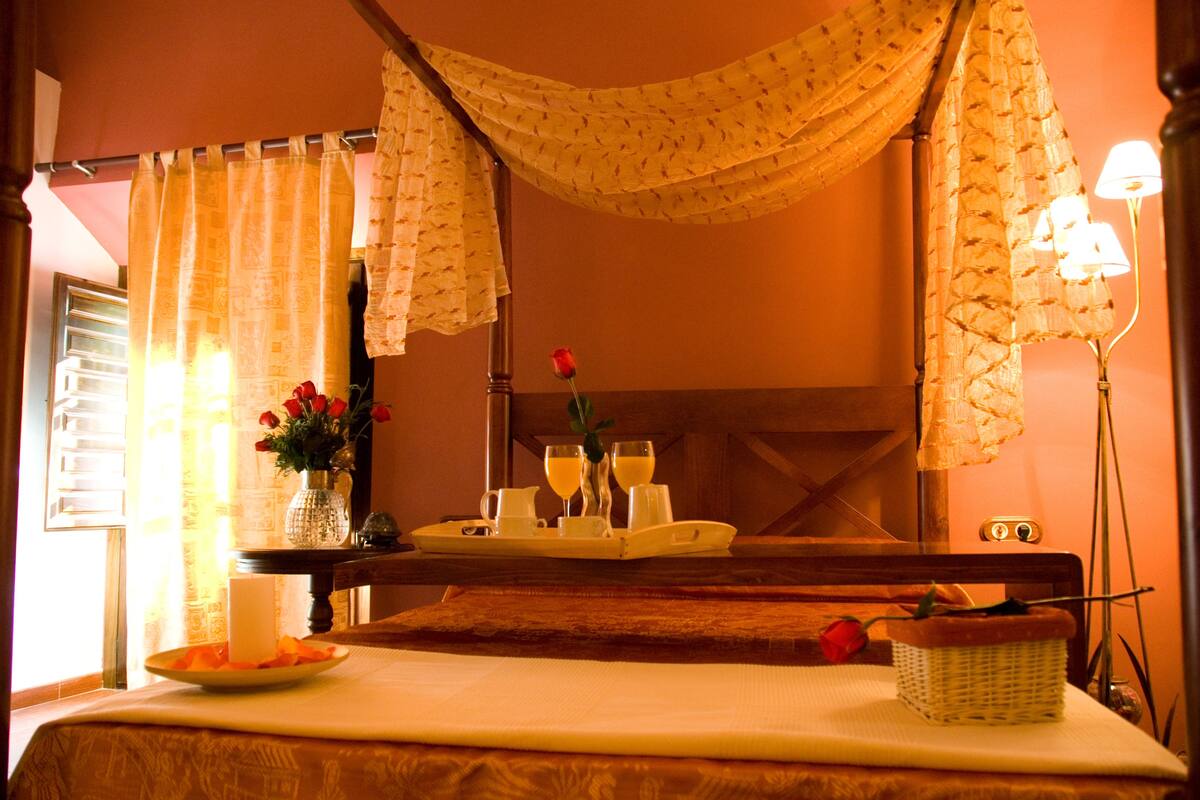 Een hotelkamer met een bed, een nachtkastje met een dienblad met ontbijtartikelen, een vaas met bloemen en een lamp.