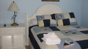 Un dormitorio con cama, mesita de noche, lámpara, ventilador de techo y un cuadro en la pared.
