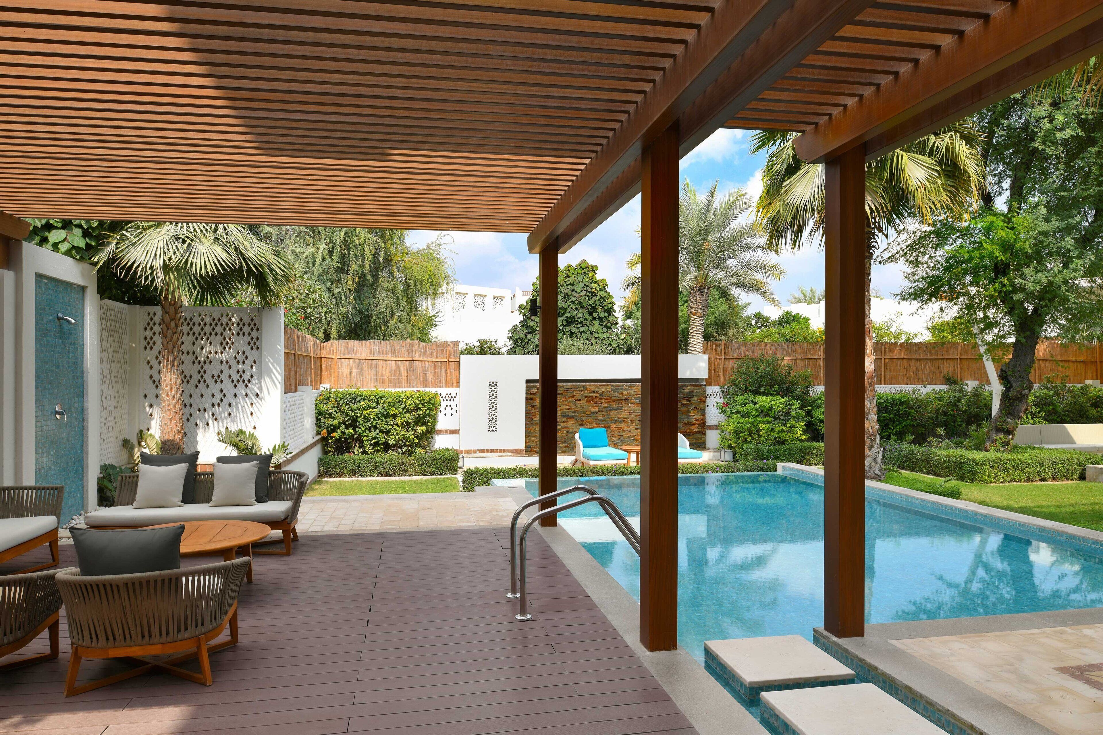 A poolside area with a wooden pergola, lounge chairs, and a pool.