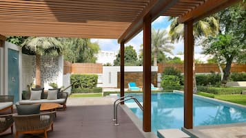 A poolside area with a wooden pergola, lounge chairs, and a pool.