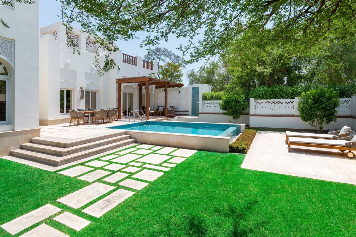 Uma área de piscina moderna ao ar livre, com pérgola, assentos e um gramado bem cuidado.
