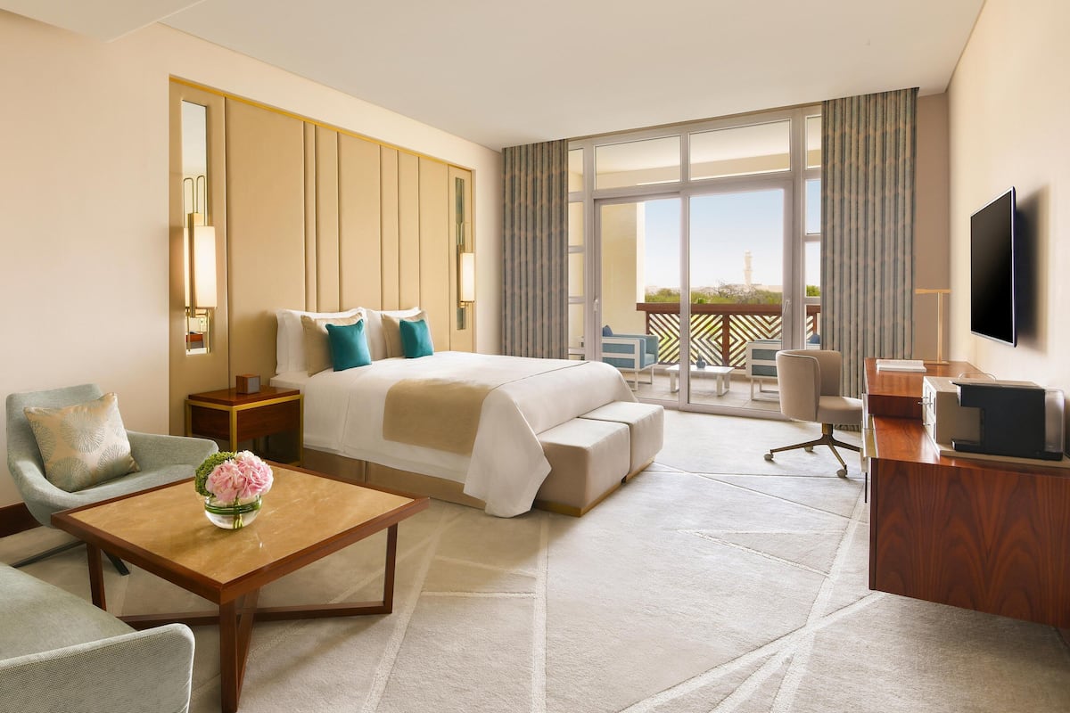 Quarto de hotel com cama, escrivaninha, televisão, cadeira e varanda com vista.