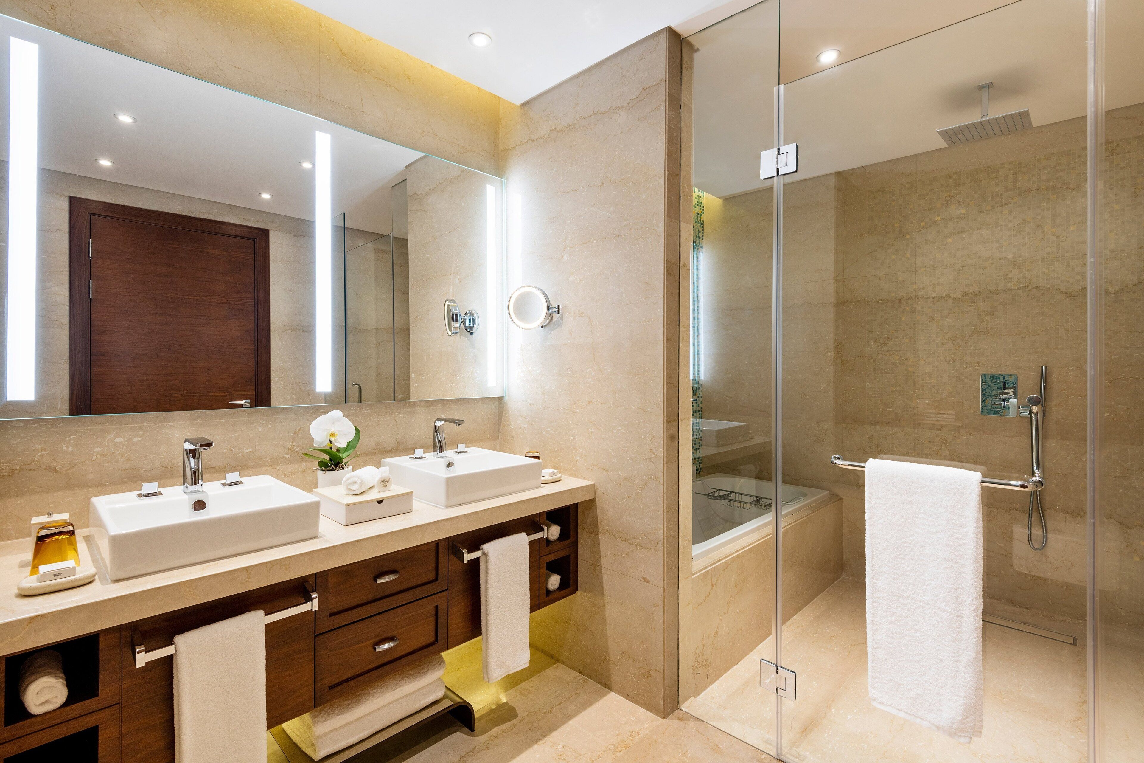 Un baño moderno con dos lavamanos, un espejo grande y una ducha con cerramiento de vidrio.