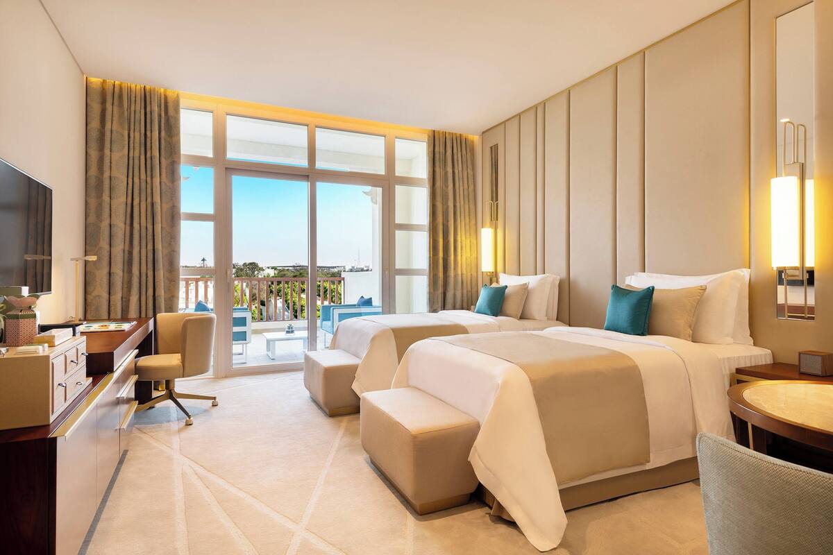Quarto de hotel com cama grande, escrivaninha, cadeira e vista para o exterior.