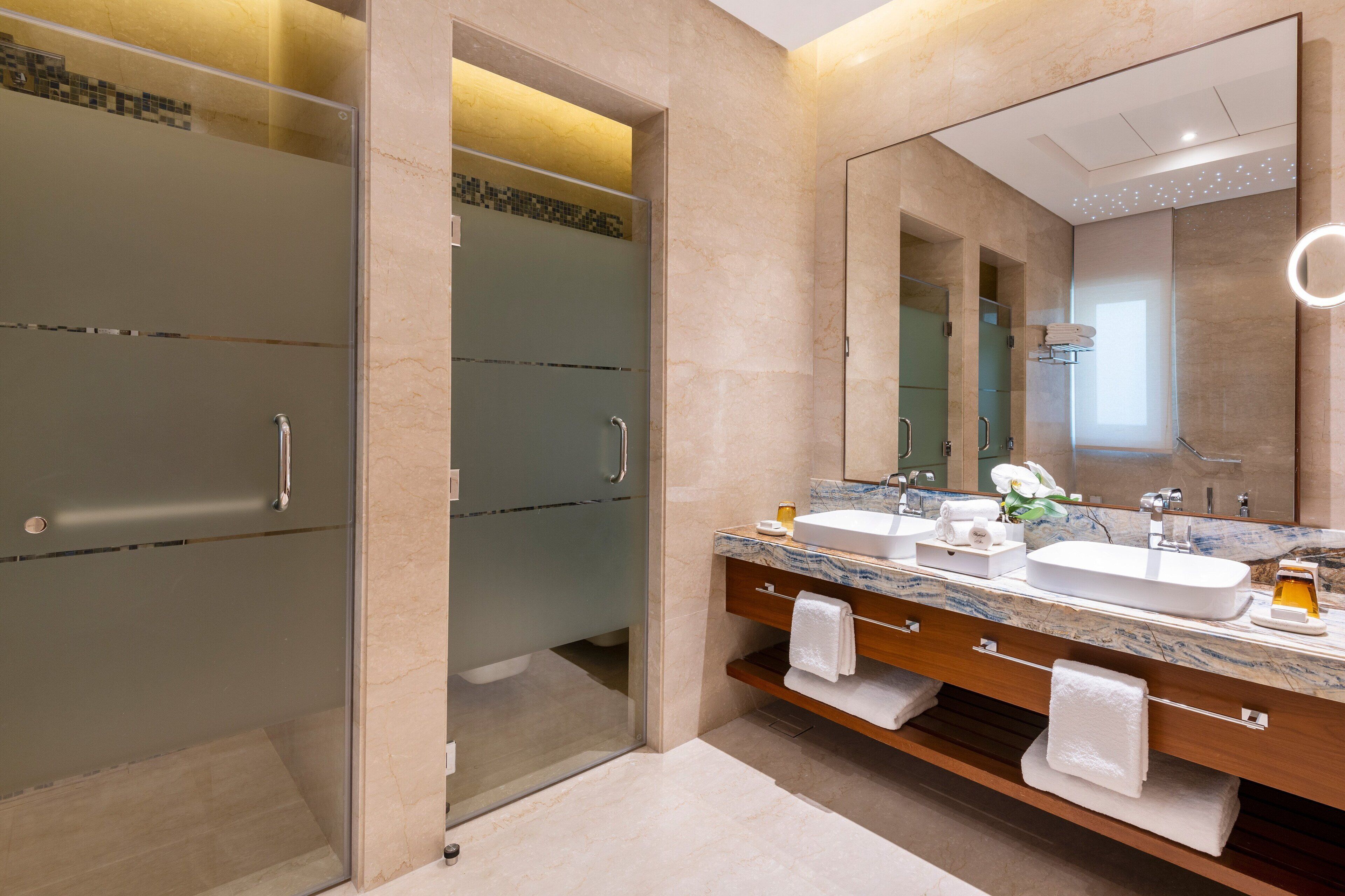 A modern bathroom with a glass shower enclosure, a marble countertop, and a large mirror.