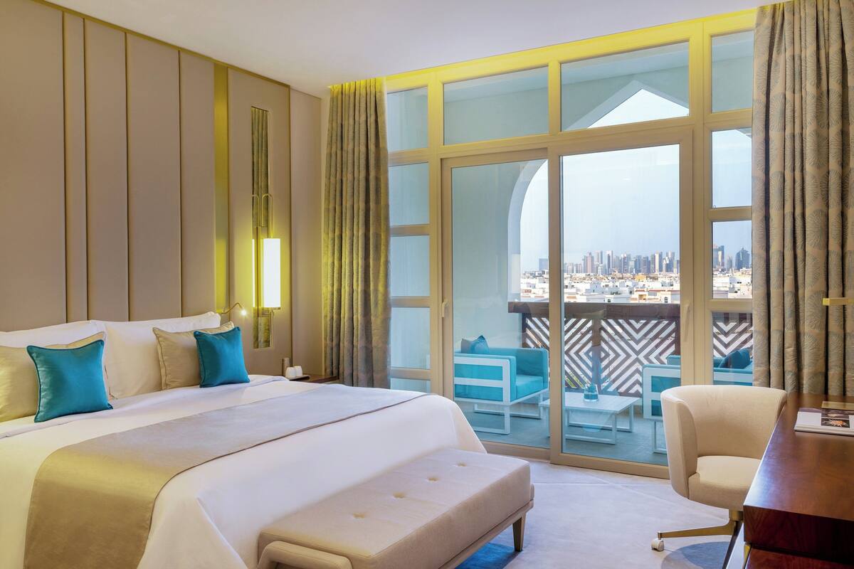 Quarto de hotel com uma cama grande, uma escrivaninha e vista para a paisagem urbana através de uma janela ampla.