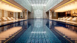 A modern hotel lobby with a central pool, wooden paneling, and seating areas.