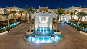A hotel entrance with a water fountain, palm trees, and a pool.
