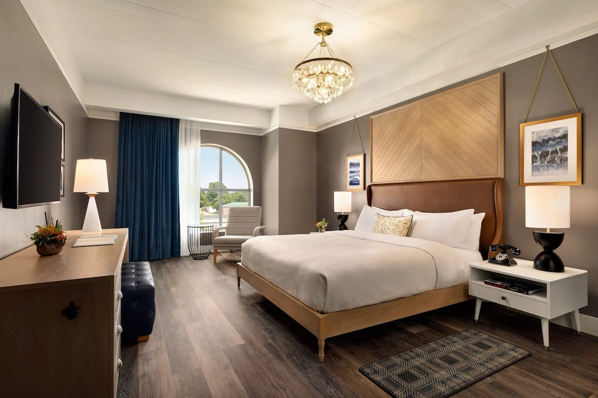 A modern hotel room with a large bed, bedside tables, a desk, and a chandelier.