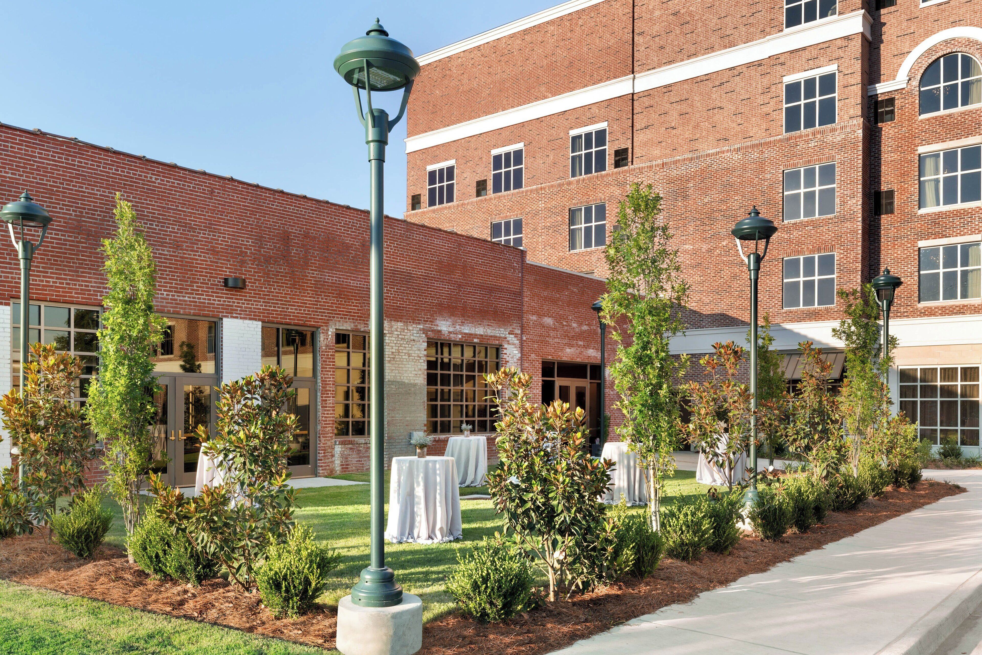 A brick building with multiple windows and a paved courtyard with tables and chairs.