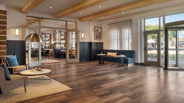A spacious living area with a wooden floor, a sofa, a coffee table, and a dining area visible through a glass door. - Cotton House, Cleveland, a Tribute Portfolio Hotel (Cleveland)