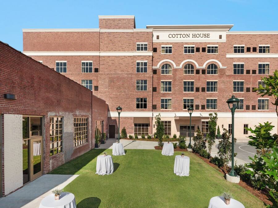 A brick building named Cotton House with a courtyard featuring four round tables with white tablecloths and potted plants.
