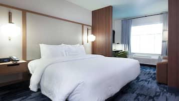 A hotel room with a large bed, bedside tables, a desk, a chair, a window with curtains, and a wall-mounted TV.