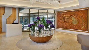 A reception area with a large wooden bowl centerpiece, a modern chandelier, and a large abstract painting on the wall. - Riyadh Diplomatic Quarter - Marriott Executive Apartments (Riyadh)
