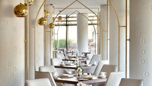 A dining area with tables set for service, white chairs, and gold accents. - Riyadh Diplomatic Quarter - Marriott Executive Apartments (Riyadh)