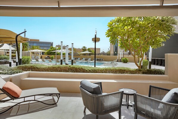 A rooftop lounge area with lounge chairs, a small table, and a view of a swimming pool and buildings in the background.