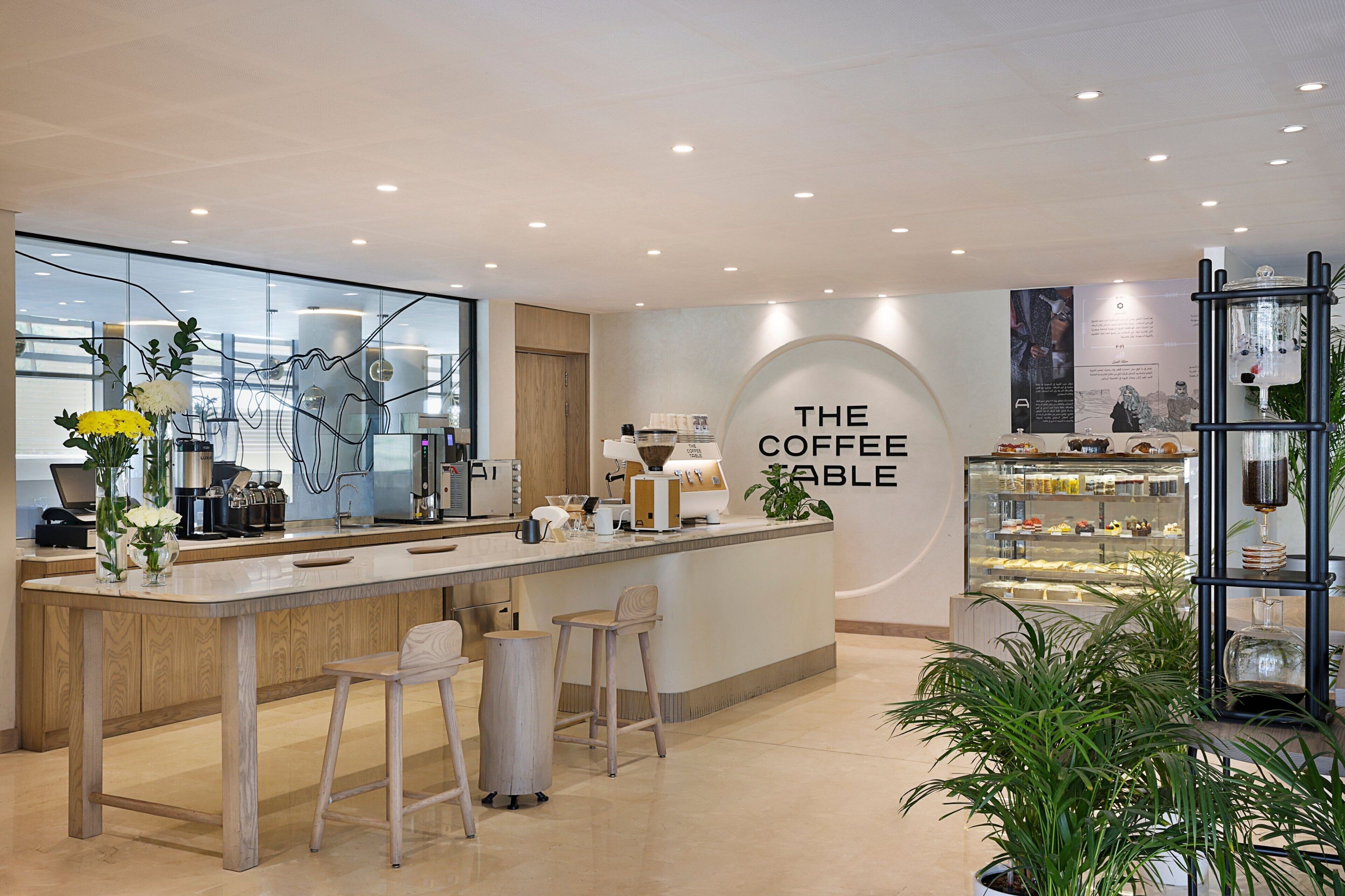 A modern coffee shop interior with a central bar, seating area, and a display case with pastries.