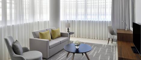 A modern living room with a grey sofa, two armchairs, a round coffee table, and a TV stand.