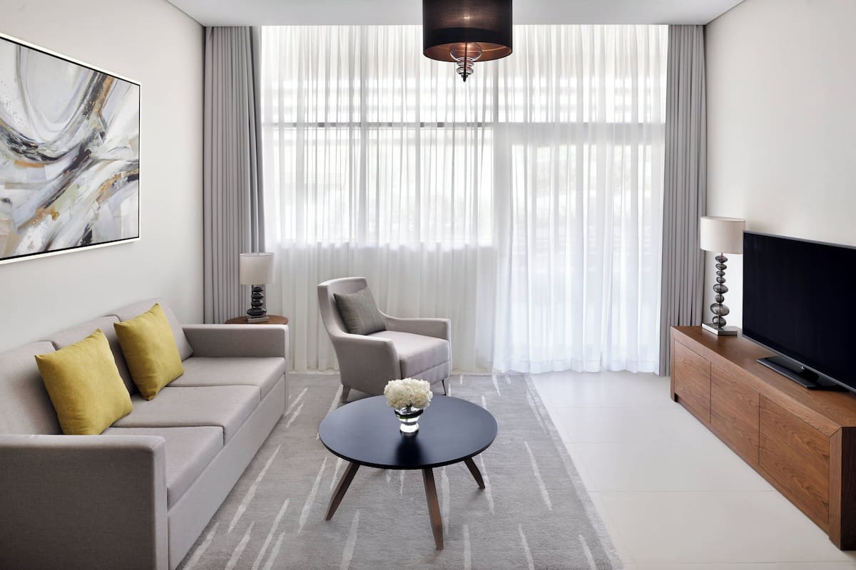 Ein modernes Wohnzimmer mit einer Couch, einem Sessel, einem runden Couchtisch und einem Fernseher auf einer Holzkommode.