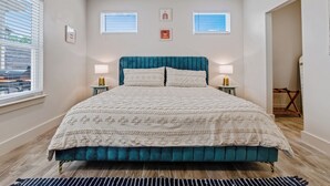 Una cama con cabecera color turquesa, ropa de cama blanca, dos lámparas de noche y vista a la calle a través de una ventana.