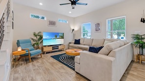 Un salon moderne avec un canapé, un téléviseur et un ventilateur de plafond.