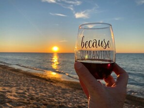 A hand holding a glass with the text "because QUARANTINE" against a sunset beach backdrop.