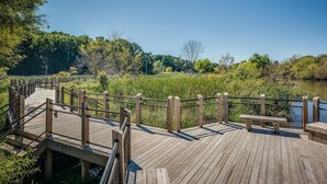 A wooden boardwalk with railings, a bench, and a clear view of a river and surrounding greenery. - Owls Nest Beach House - Just Steps From Our Private Beautiful Sandy Beach (Union Pier)