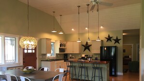 A spacious kitchen with a central island, white bar stools, and pendant lighting. - Owls Nest Beach House - Just Steps From Our Private Beautiful Sandy Beach (Union Pier)