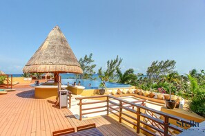 A wooden deck with a thatched-roof structure, a pool, and outdoor seating. - Pueblito Escondido Condos by Stella Rentals (Playa del Carmen)