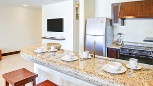 Una cocina moderna con encimeras de granito, un refrigerador de acero inoxidable, una estufa y un televisor de pantalla plana montado en la pared.